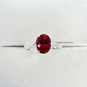 Peut inclure: Une bague en argent ornée d'une grosse pierre rouge foncé de forme ovale. La monture de la bague présente un motif délicat en forme de branche. Le texte "zkgemsjewellery" est visible.