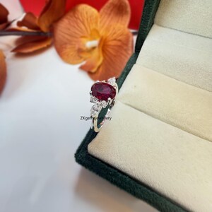 May include: A silver ring featuring a large oval ruby gemstone surrounded by smaller diamonds. The ring is set in a delicate floral design.