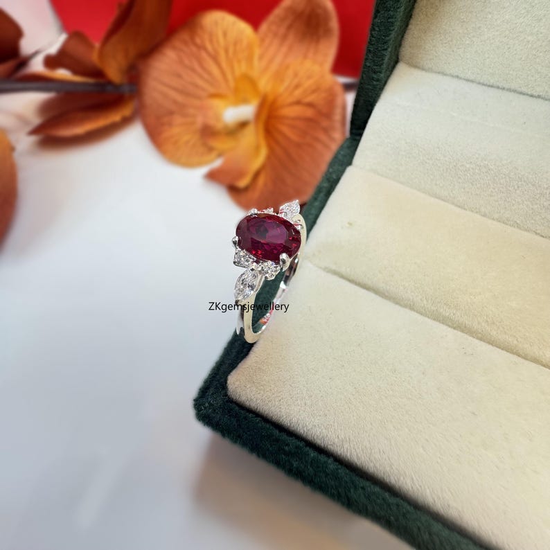 May include: A silver ring featuring a large oval ruby gemstone surrounded by smaller diamonds. The ring is set in a delicate floral design.