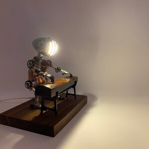 May include: A steampunk-style lamp shaped like a robot playing a zither. The robot is made of copper and metal, and the zither is made of wood. The lamp is on a wooden base.