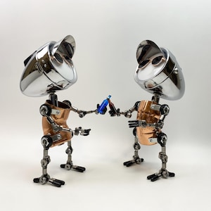 Peut inclure: Deux sculptures de robots, chacune avec une tête chromée, un torse en cuivre et des membres articulés, sont représentées en train de trinquer avec de petites bouteilles. Les robots se tiennent sur une surface blanche, créant une esthétique ludique et industrielle.