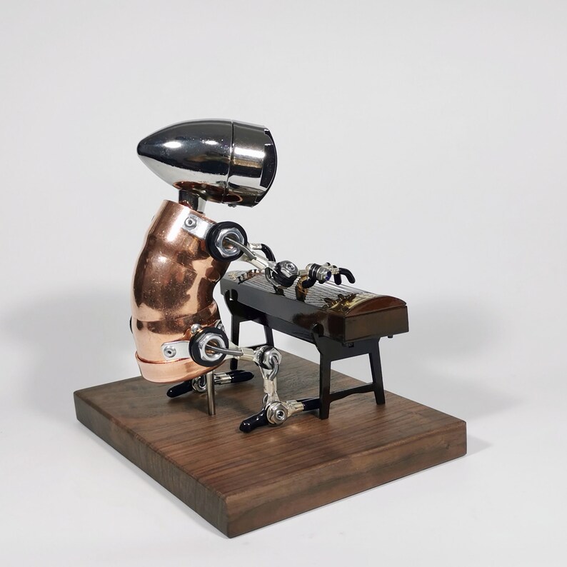 May include: A silver and copper robot playing a black and gold zither on a wooden platform.