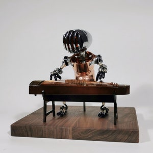May include: A small, silver and copper robot plays a traditional Chinese zither, or guzheng, on a wooden stand. The robot has a silver head with a grill-like design and copper body. The zither is brown with a black stand.