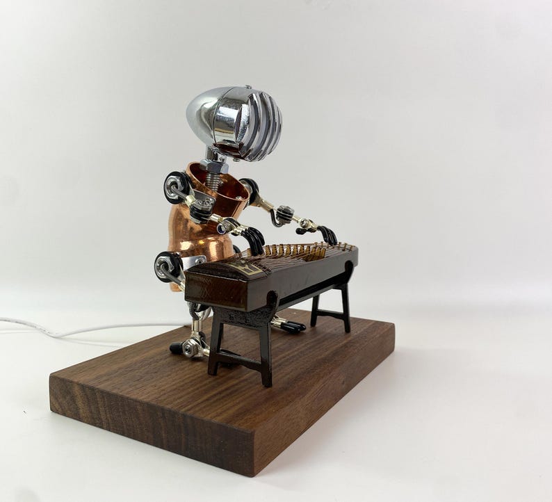 May include: A robot made of metal and copper plays a zither, a traditional Chinese musical instrument. The robot is sitting on a wooden base.