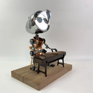 May include: A silver robot with sunglasses plays a dark brown zither on a wooden platform. The robot is made of recycled materials and has a copper torso.