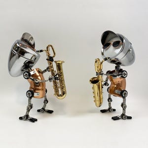 Peut inclure: Deux sculptures originales de musiciens. Chaque figurine est faite de composants métalliques, avec une tête chromée brillante et un torse cuivré. L'une joue du saxophone doré. L'autre porte des lunettes de soleil et joue du saxophone doré.