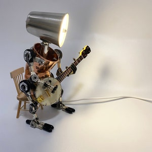 May include: A silver lamp with a copper body and a banjo attached to it. The lamp is on a wooden stool.