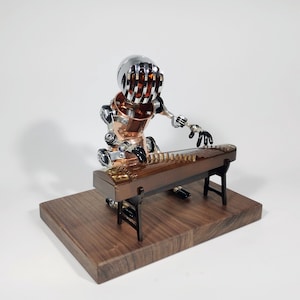 May include: A steampunk-style robot made of metal and copper plays a traditional Chinese zither, or guzheng, on a wooden platform. The robot has a silver helmet with a wire mesh design and is wearing a copper body. The zither is brown with a gold trim and has 21 strings.