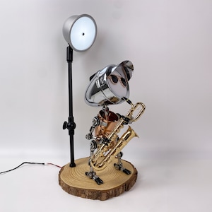May include: A silver robot with sunglasses playing a gold saxophone on a wooden base. A silver lamp with a white light shade is in the background.