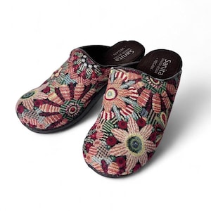 May include: A pair of Sanita vegan clogs featuring a woven fabric upper with a multi-colored floral pattern in shades of red, pink, green, and blue. The interior footbed is black and displays the Sanita brand name and the word vegan in white text.