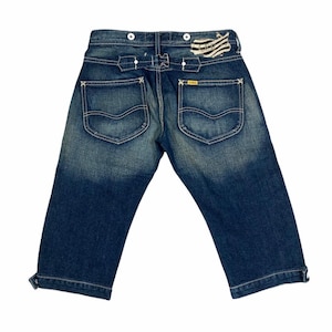 May include: Blue denim shorts with a distressed look, featuring a unique button closure and a patch on the back with a striped design. The shorts have two back pockets with a yellow label.