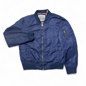 May include: A navy blue bomber jacket with a zip-up front, ribbed cuffs, and a small zip pocket on the left sleeve. The jacket has a classic bomber style with a collar and a Levi Strauss & Co. label.