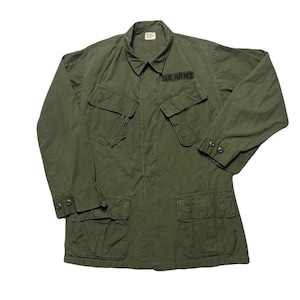 Op de afbeelding: Een groene militaire jas met vier grote zakken en een patch met de tekst "US ARMY".