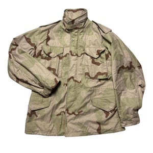 May include: A tan, brown and green camouflage jacket with a button-up front and two large pockets on the front.