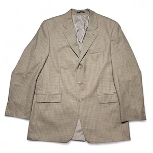 Può includere: Un blazer beige con un sottile motivo a quadri. La giacca ha una chiusura a tre bottoni, due tasche anteriori e un risvolto a lancia. La fodera interna è di colore grigio chiaro.