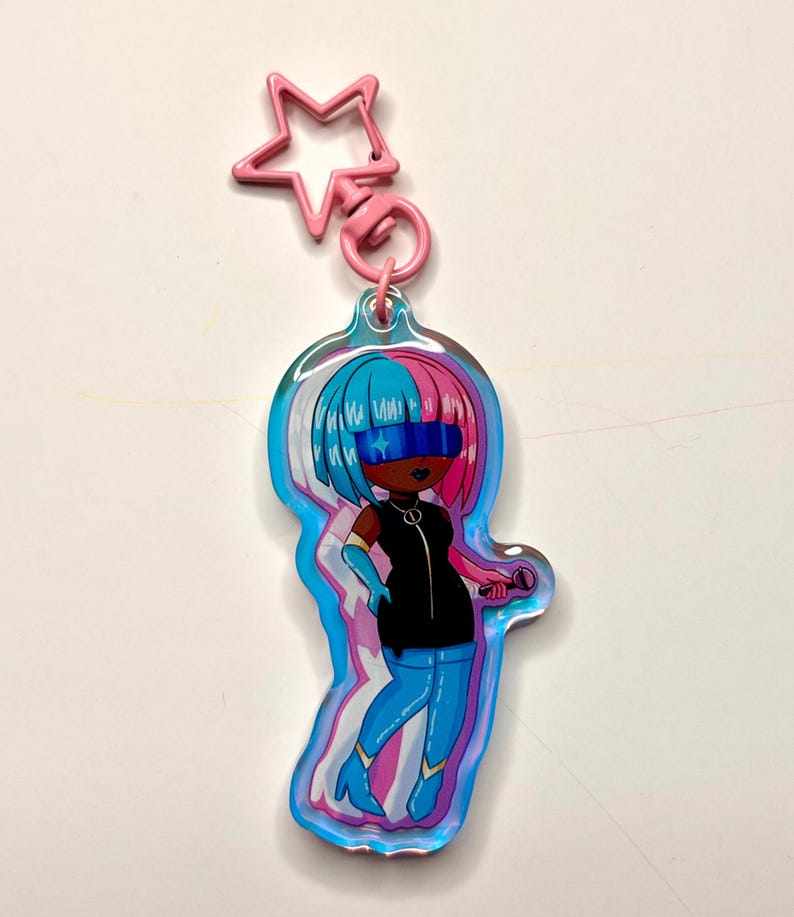May include: A colorful keychain featuring a cartoon character with blue and pink hair, wearing a black outfit and blue boots. The keychain has a pink star-shaped clasp and a silver ring. The character is holding a microphone.