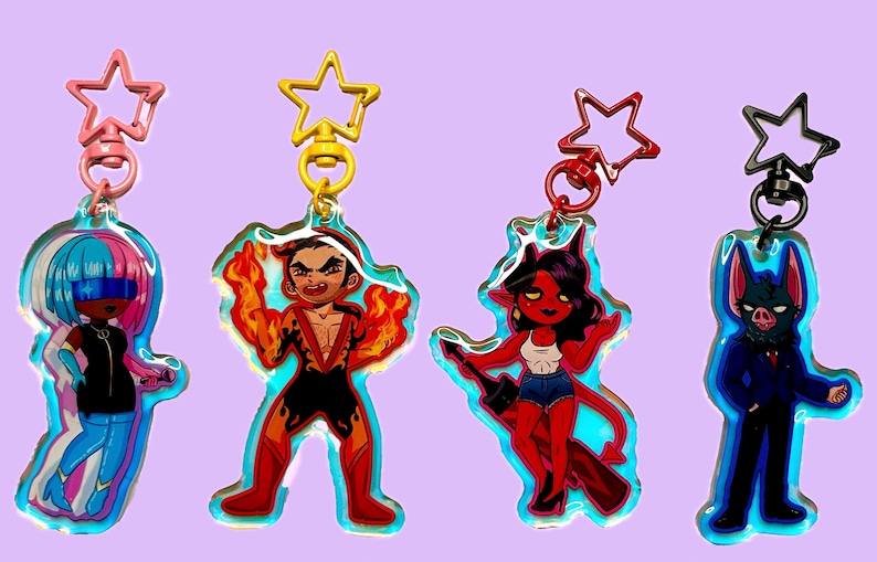 May include: Four acrylic keychains featuring cartoon characters with star-shaped clasps. The characters include a figure with blue and pink hair, a man engulfed in flames, a red-skinned demon, and a bat-like creature, all on a lavender background.