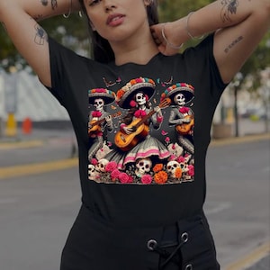 May include: Black t-shirt with a graphic of three skeleton musicians wearing sombreros and playing guitars. The skeletons are surrounded by flowers and skulls.