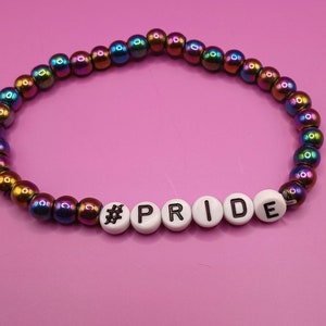 Peut inclure: Un bracelet de perles de couleur arc-en-ciel avec des perles de lettres blanches qui épellent "#PRIDE".