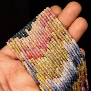 May include: A collection of multi-colored gemstone beads arranged in long, thin strands. The beads feature a faceted texture and a gradient of colors including shades of blue, yellow, pink, and clear, creating a vibrant, translucent appearance.