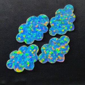 May include: Four cloud-shaped cabochons made of synthetic opal. Each piece features a vibrant blue base colour with scattered, iridescent flashes of green, yellow, and orange throughout the surface, creating a bright, multi-coloured mosaic effect.