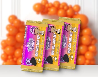 May include: Three gold chocolate bar wrappers with pink and purple glitter accents. The wrappers feature a cartoon image of a baby with a question mark and the text "The Proud Family, Who Will Baby Be? Gender Reveal".