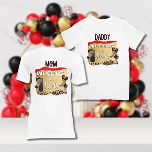 Könnte beinhalten: Zwei weiße T-Shirts mit einem roten und goldenen Grafikdesign. Die Grafik zeigt einen Reifen und zwei Comic-Babys mit dem Text "Räder oder Absätze" und "Mama" oder "Papa".