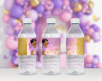 May include: Three clear plastic water bottles with labels featuring a pink and gold design. The labels have a picture of a young girl with butterfly wings and the text "A new little butterfly is on the way".