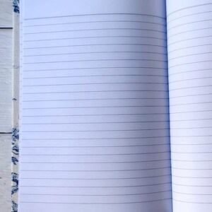 May include: An open notebook with lined pages. The cover is made of a white fabric with a blue floral pattern.