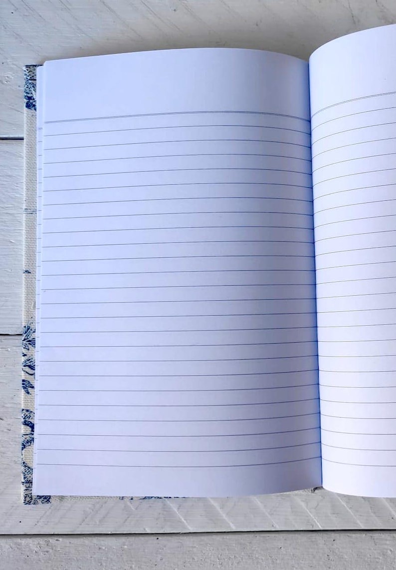 May include: An open notebook with lined pages. The cover is made of a white fabric with a blue floral pattern.