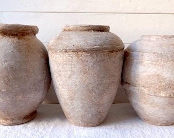 May include: Three white ceramic pots with a rustic, textured finish. The pots are different sizes and shapes, and they are all slightly weathered.