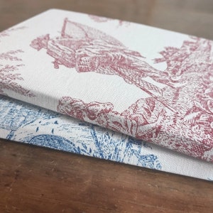 May include: Two fabric-covered journals with a vintage floral design. The top journal has a red floral pattern, and the bottom journal has a blue floral pattern.