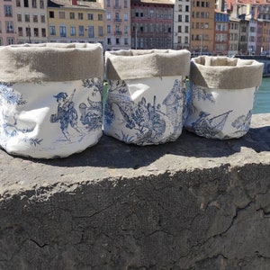Op de afbeelding: Drie witte stoffen opbergmanden met blauw-witte patronen. De manden hebben een linnen bovenkant en staan op een grijs stenen oppervlak.