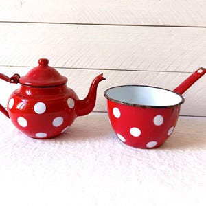 Può includere: Teiera e pentola di smalto rosso con pois bianchi. Entrambe sono vintage e hanno un aspetto rustico.