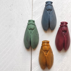 Può includere: Quattro figurine di cicala decorative in diversi colori: blu, verde, rosso e giallo. Le cicale sono realizzate in un materiale liscio dipinto e hanno una forma realistica.