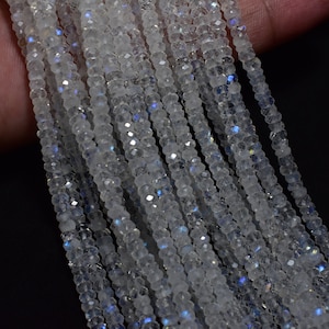 May include: A strand of white moonstone beads with iridescent blue and purple flashes. The beads are faceted and have a smooth, polished finish.