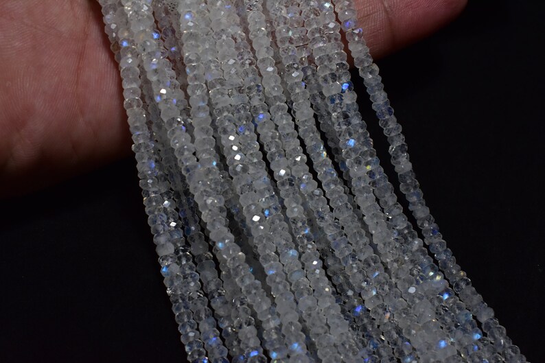 May include: A strand of white moonstone beads with iridescent blue and purple flashes. The beads are faceted and have a smooth, polished finish.
