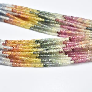 May include: Close-up of multiple strands of colourful gemstone beads. The beads are small and faceted, displaying a range of colours including yellow, orange, pink, green, and grey. The beads are strung together, creating a textured and vibrant appearance. Ideal for jewellery making.
