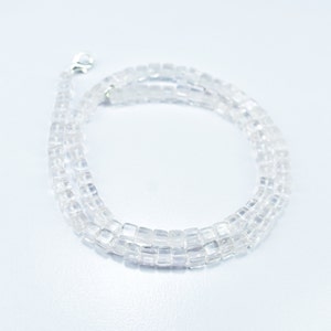 Puede incluir: Un collar de cristal transparente hecho de cuentas cuadradas. El collar está en capas y tiene un cierre plateado.