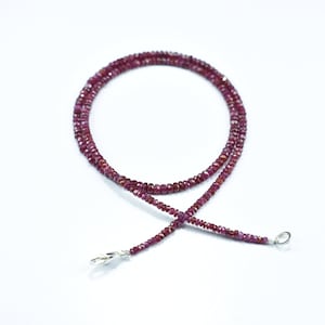 Könnte beinhalten: Eine lange Halskette aus kleinen, facettierten Rubinperlen. Die Kette ist auf einer silbernen Kette aufgefädelt und hat einen silbernen Verschluss.