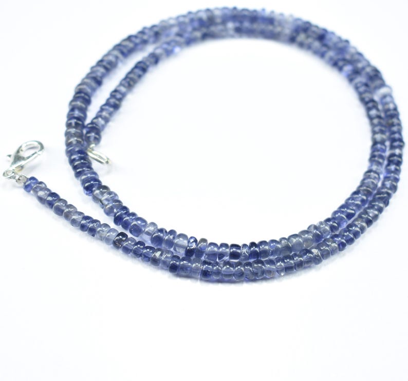 K&ouml;nnte beinhalten: Eine Halskette aus kleinen, runden, blau-violetten Perlen. Die Perlen sind zu einer zarten Kette aufgereiht. Ein silberfarbener Verschluss ist an einem Ende befestigt. Die Halskette wird vor einem wei&szlig;en Hintergrund gezeigt.