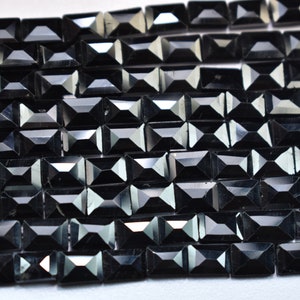 May include: Close-up of a collection of black rectangular beads. Each bead has a faceted surface, creating multiple reflective surfaces. The beads are arranged in rows, suggesting they are strung together for jewelry making.