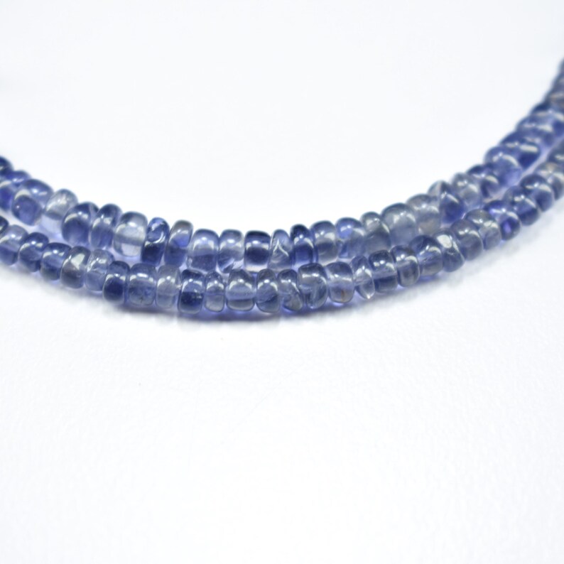 K&ouml;nnte beinhalten: Drei Str&auml;nge aus blau-violetten Edelsteinperlen. Die Perlen sind klein, abgerundet und haben eine leicht unregelm&auml;&szlig;ige Form. Der Hintergrund ist schlicht wei&szlig; und hebt die Farbe und Textur der Perlen hervor. Die Perlen sind aufgef&auml;delt, was darauf hindeutet, dass sie f&uuml;r Schmuckzwecke bestimmt sind.