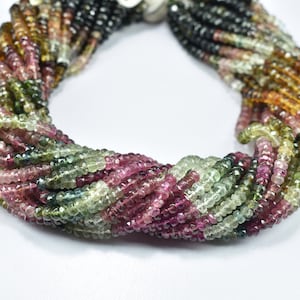 Può includere: Una collana a più fili composta da piccole pietre preziose sfaccettate in una varietà di colori, tra cui rosa, verde, giallo e nero. Le perline sono infilate insieme, creando un effetto corda attorcigliata. La collana è esposta su sfondo bianco.