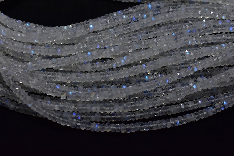 May include: A strand of white moonstone beads with iridescent blue flashes. The beads are faceted and have a smooth, polished finish.