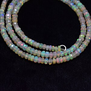 May include: A strand of white opal beads with iridescent rainbow colors. The beads are faceted and have a slightly irregular shape. The strand is layered and appears to be a necklace.