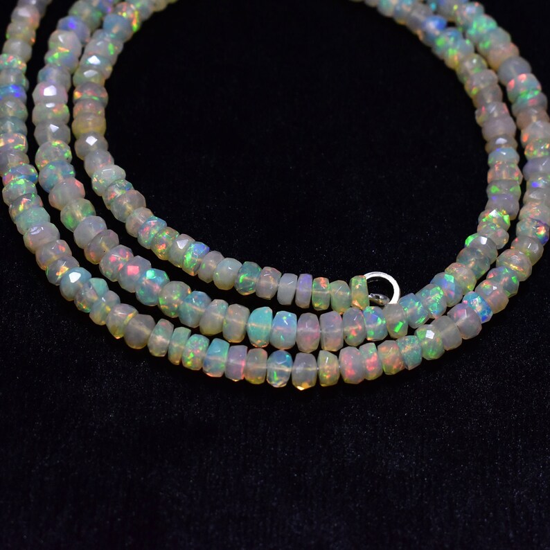 May include: A strand of white opal beads with iridescent rainbow colors. The beads are faceted and have a slightly irregular shape. The strand is layered and appears to be a necklace.