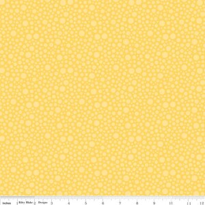 May include: A yellow fabric featuring a repeating pattern of light yellow circles of varying sizes, resembling bubbles. A white ruler at the bottom edge shows measurements in inches, with the text Riley Blake Designs printed clearly.