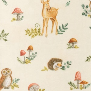 May include: A cream-colored fabric featuring a repeating pattern of woodland creatures and plants. The design includes a deer, owl, hedgehog, mushrooms, and various green foliage. The illustrations are in soft, muted colors.