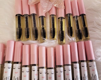 Könnte beinhalten: Eine Sammlung von 18 rosa Flaschen mit klarer Flüssigkeit und einem schwarzen Applikatorpinsel. Jede Flasche hat ein weißes Etikett mit dem Text "Cuu latte's Eyebrows & Eyelash Glowth Serum Castor Oil, Jojoba Oil & Vitamin E 10ml".